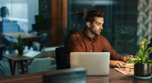 Businessman,Going,Over,Paperwork,And,Using,A,Laptop,While,Working